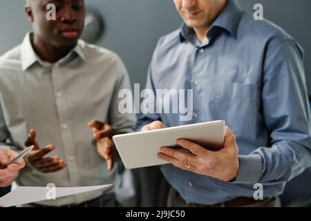 Selective focus shot of modern trading specialists standing in office analyzing currency value watching stats on tablet Stock Photo
