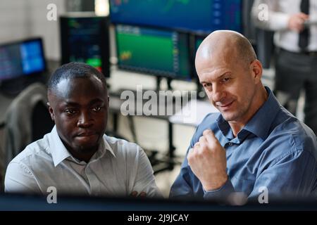 High angle view of two men working in stock trading and investment company watching charts and graphs of currency on monitor in office Stock Photo