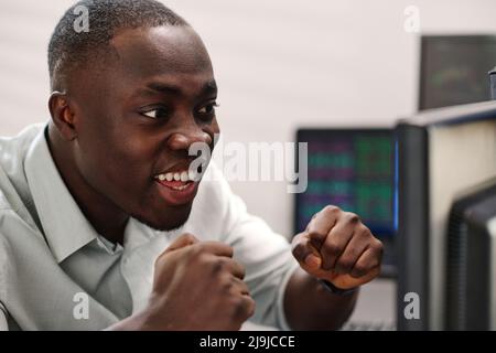 Close-up of cheerful African American man in formalwear looking at computer screen watching stock trading stats growth and feeling happiness Stock Photo