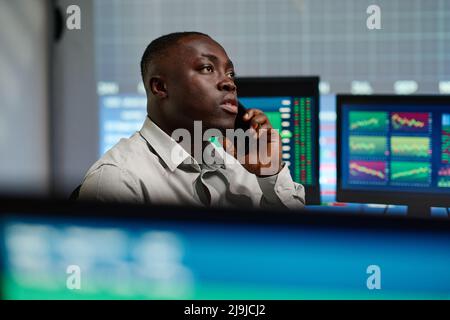 Modern young African American man in formalwear working in brokerage company spending evening in office having phone call with investor Stock Photo