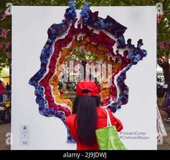 London, UK. 23rd May, 2022. A woman takes a photo of 'The Queen's Head' flower display on Sloane Square during the free floral art show Chelsea In Bloom. Shops, hotels and restaurants in London's Chelsea area are taking part in the annual competition, and the 2022 theme is 'British Icons'. Credit: SOPA Images Limited/Alamy Live News Stock Photo
