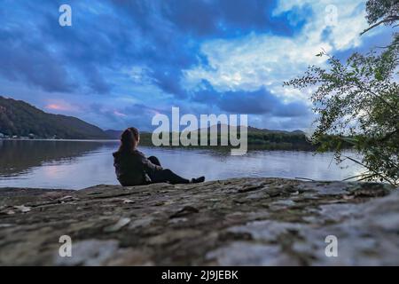 Woman sitting on rock admiring view of the Hawkesbury river on the NSW central coast of Australia at sunset Stock Photo