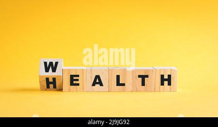 Wooden cube blocks flip from wealth to health wording. On yellow background. Stock Photo