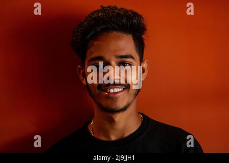 Biometric verification. Human facial detection, high technology. Indian man student holding phone face ID scanning orange wall background Stock Photo