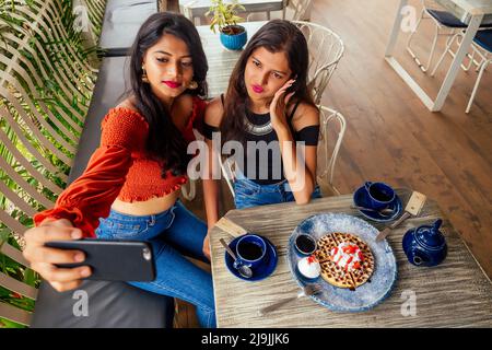 fashionable indian friends couple of two woman making selfie mobile phone.friends long-awaited meeting gossip students eating pancake drinking masala Stock Photo