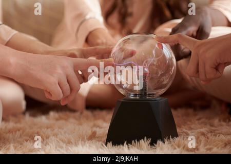 Hands of young women touching plasma ball with smooth purple and pink flames Stock Photo