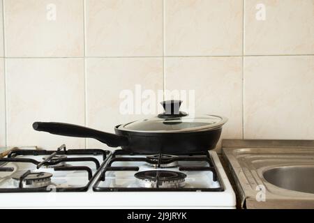 A frying pan stands on a gas stove at home in the kitchen, kitchen utensils and household appliances, cooking Stock Photo