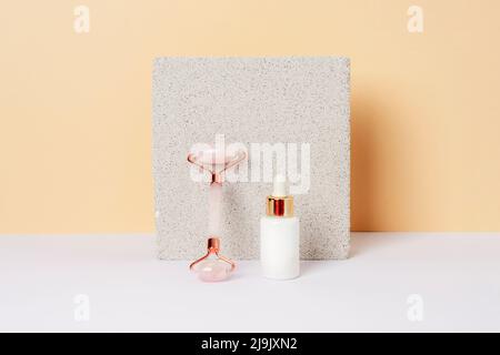 White serum bottle and crystal rose quartz facial roller, natural skin care products and tools on the natural stone background against yellow wall on Stock Photo