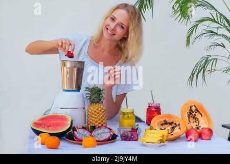 Young happy woman with fresh juice mix fruit making healthy drinks on juicer smoothie jar on a white background summer tropical vacation in warm Stock Photo