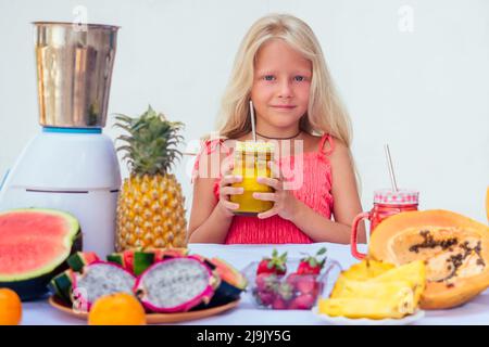 caucasian family in the kitchen during breakfast at home. two blonde sisters cooking smoothies in a blender.tropical summer theme Stock Photo