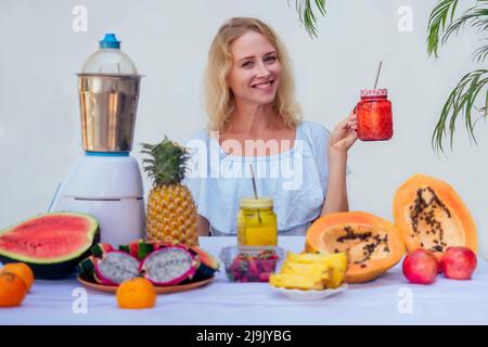 Young happy woman with fresh juice mix fruit making healthy drinks on juicer smoothie jar on a white background summer tropical vacation in warm Stock Photo