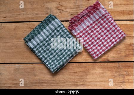 Multicolored kitchen napkins or towels lie on a wooden surface. Red and green checkered napkins. Top view. Stock Photo