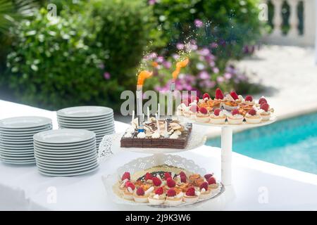 Dessert buffet, small chocolate and strawberry cakes, birthday candles by the pool. Stock Photo