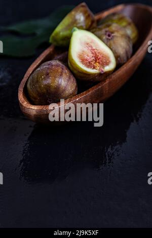 Figs with leaves in a wooden plate on a black background. Stock Photo
