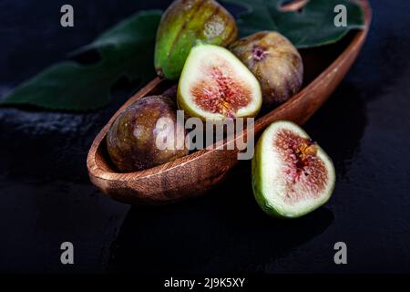 Figs with leaves in a wooden plate on a black background. Stock Photo