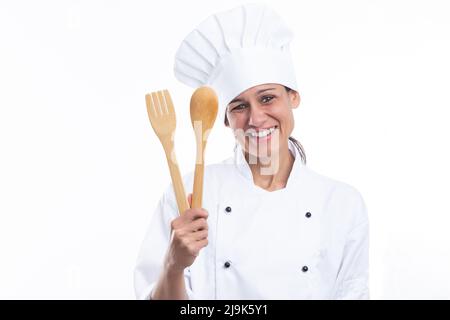 Portrait of positive caucasian woman in chef's outfit with kitchen tools in hands looking at camera isolated on white background. Stock Photo