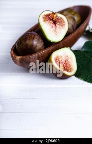 Figs with leaves in a wooden plate on a white wooden background. Stock Photo