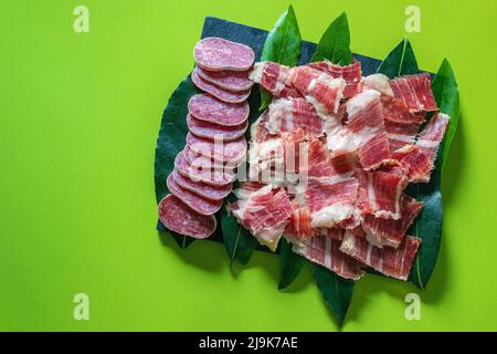 Fuet, Sausage sliced and Iberian spanish ham on green background. Spanish sausage. Gastronomy and food in Spain.Traditional Spanish Jamon Serrano ham. Stock Photo