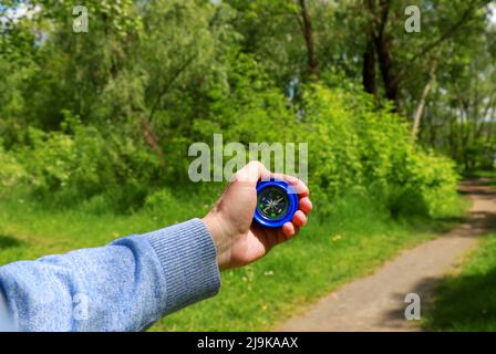 A tourist holds compass in his hand against background of green trees in forest. Travel, hiking and trekking concept. Summer, spring vacation, recreat Stock Photo