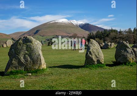 People tourists walkers at Castlerigg Stone Circle, snow topped Blencathra in background spring late winter Lake District National Park England UK Stock Photo