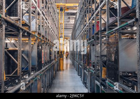 Interior of modern storage warehouse with coils of colored cable on metal shelves. Forklift lift at plant. Stock Photo