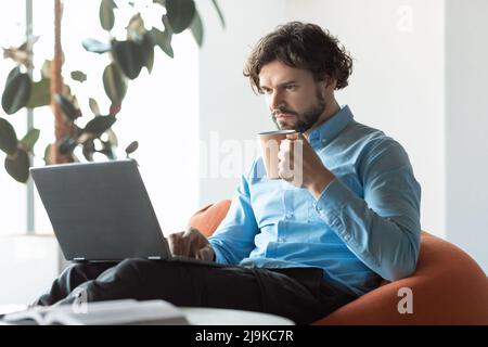 Business man using pc sitting on chair drinking coffee Stock Photo