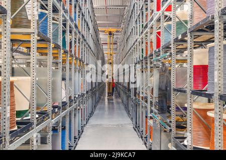 Interior of modern storage warehouse with coils of colored cable on metal shelves. Forklift lift at plant. Stock Photo
