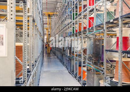 Interior of modern storage warehouse with coils of colored cable on metal shelves. Forklift lift at plant. Stock Photo