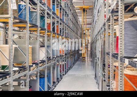 Interior of modern storage warehouse with coils of colored cable on metal shelves. Forklift at plant. Stock Photo