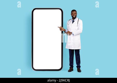 African American Male Physician In White Uniform Pointing At Big Phone Screen Stock Photo