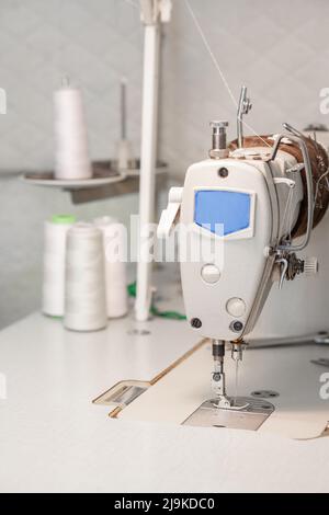 Sewing machine close-up on the background of coils with white threads. Stock Photo