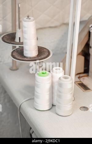 Reels with white threads for a sewing machine on a stand in atelier. Stock Photo