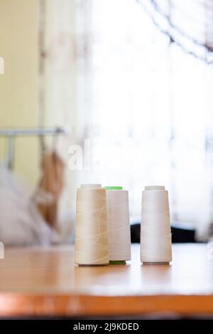 Reels with white threads for a sewing machine on a polished wooden table in atelier Stock Photo