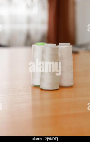 Reels with white threads for a sewing machine on a polished wooden table in atelier Stock Photo