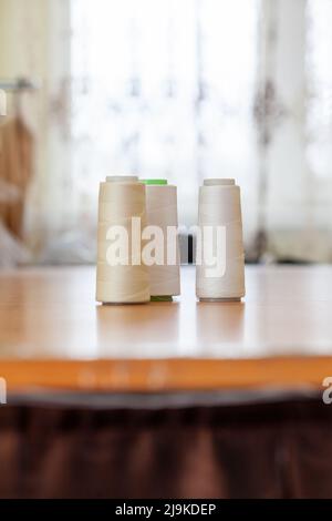 Reels with white threads for a sewing machine on a polished wooden table in atelier Stock Photo
