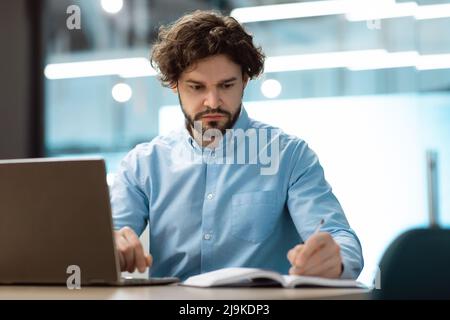Portrait of focused businessman using laptop and writing Stock Photo