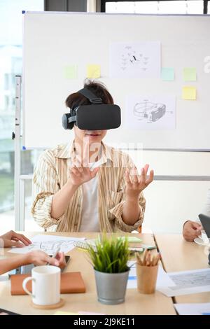Portrait of an Asian millennial male tech developer testing his new virtual innovation with VR glasses in the meeting. Stock Photo
