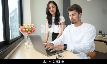 An Asian millennial man and woman collaborate on project campaign and marketing advertisement, working together in the office. Stock Photo