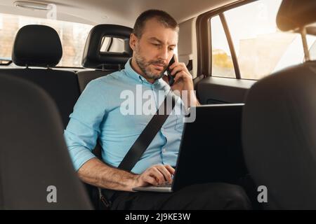 Businessman using laptop talking on smartphone while going by car Stock Photo