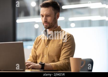 Male Office Worker Working On Laptop Sitting At Workplace Indoor Stock Photo