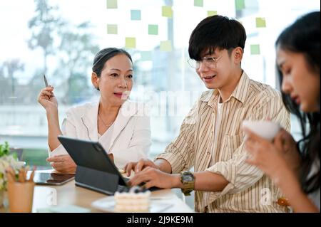 Asian senior female manager working with a younger graphic designer team in the office workplace. Stock Photo