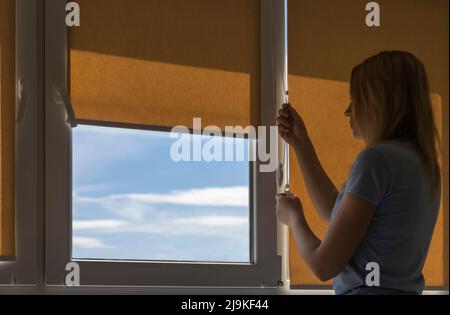 Silhouette of a woman opening the blinds on a sunny morning. Stock Photo
