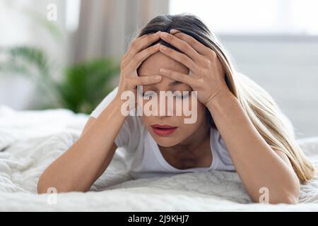 Unhappy blonde woman suffering from migraine, home interior Stock Photo