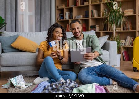 Stylish african american couple preparing for vacation, woman holding passports and man using tablet Stock Photo