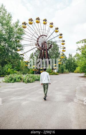 young male tourists walking in front of the abandoned ferris wheel amusement park in Pripyat Chernobyl Stock Photo