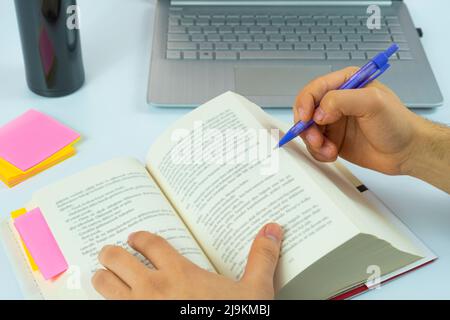 Laptop and open book with purple pencil isolated on white background, studying and working concept, focus on reading, taking note, sitting view Stock Photo