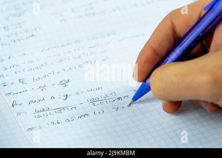 Mathematical numbers on a notebook and man hand holding purple pencil, studying math concept, focus on solution idea, sitting view Stock Photo