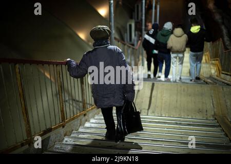 Pensioner goes down stairs in evening. Old woman walks down steps. Woman is holding on to railing. Stock Photo