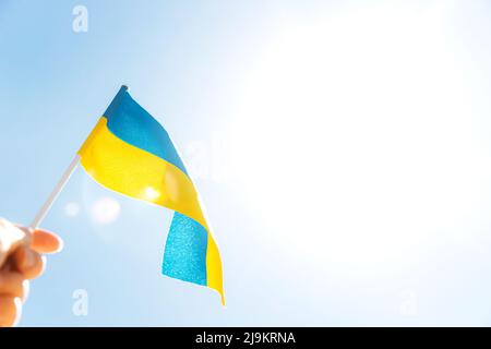 Human hand holding large bicolor yellow blue Ukrainian state flag, national symbol fluttering, waving in wind against blue sky on sunny day. Ukraine Independence Constitution Day, National holiday Stock Photo