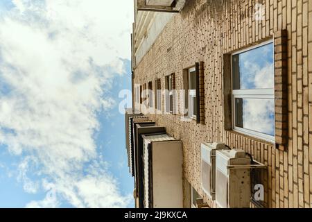 Low angle view of residential yellow house with balconies, windows and drainpipe. Blue sky with clouds. Air conditioner hangs on facade of house. Stock Photo